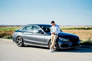 20 25 Prints: Young businessman leaning against car on country road using smartphone