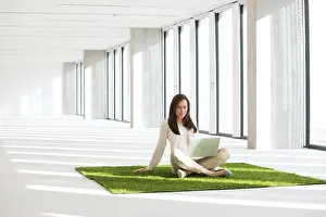 25 29 Years Prints: Young businesswoman with laptop sitting on turf in empty office