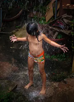 Preschooler Prints: A young Cambodian Khmer child cools herself in rainwater pouring from a downspout in Siem Reap