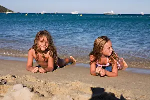 Cote Dazur Prints: Young caucasian girls lying on the sand waiting for the waves