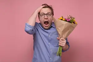 Gerbera Prints: Young caucasian man in glasses having surprised face with flowers for his girlfriend for birthday gift
