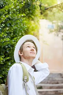 A young Caucasian man in a white hat walks along the street of the old city. Anafiotika. Athens. Greece