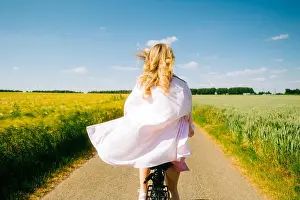 Outdoor Recreation Prints: Young caucasian woman with blond hair riding among agricultural fields in countryside in summer day