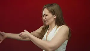 Pulling Prints: Young caucasian woman pulls arms forward while smiling in red studio wearing white sleeveless top; determination