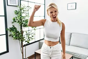 Fist Prints: Young caucasian woman standing at living room angry and mad raising fist frustrated