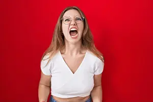 Enraged Prints: Young caucasian woman standing over red background angry and mad screaming frustrated and furious