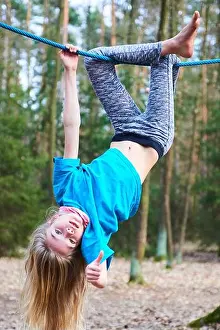 Active Prints: Young child girl hanging on rope upside down on playground in park