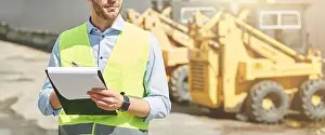 Vest Prints: Young civil engineer wearing helmet writing report while standing at construction site