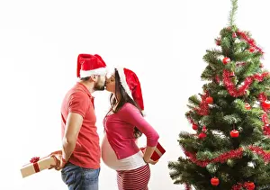 Close To Prints: Young couple is dancing close to christmas tree. Woman is pregnant