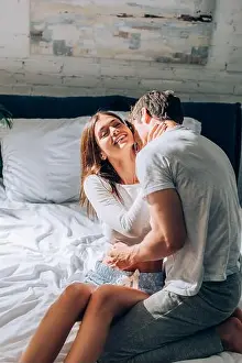Pajamas Prints: Young couple in pajamas sitting on bed and touching each other