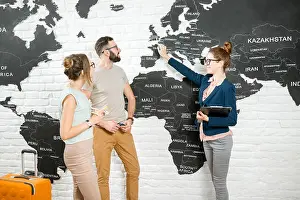 Choosing Prints: Young couple of travelers choosing a summer trip with travel agent pointing on Great Britain on the world map