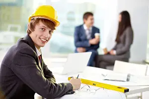 White Collar Prints: Young engineer looking at camera with his colleagues on background