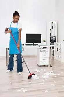 Housekeeper Prints: Young Female Janitor Sweeping Torn Paper Pieces On Hardwood Floor