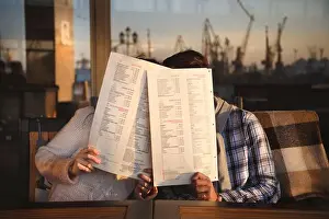 Kissing Prints: Young funny happy loving couple sitting at sea port open-air cafe and kissing closing their faces with menus