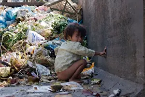 Litter Prints: A young girl is defecating in a dumpster filled with garbage on a trash strewn street in Phnom Penh