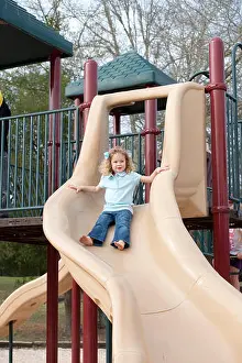Curly Hair Prints: Young girl goes down slide at park playground