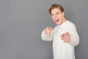 Knitted Prints: Young guy wearing stylish white sweater studio isolated on grey wall pointing at camera shouting joyful side view