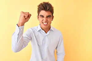 Punching Prints: Young handsome businessman wearing elegant shirt over isolated yellow background angry