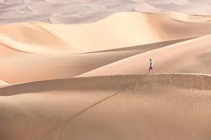 Young handsome caucasian tourist in shorts and straq hat hiking in Liwa desert dunes. Abu Dhabi, UAE