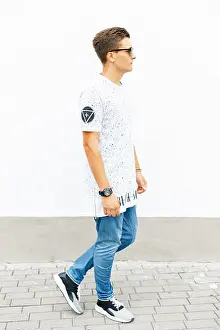 Sneakers Prints: Young handsome man in a white T-shirt, blue jeans and sneakers standing near a white wall