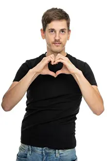 Fashion Model Prints: Young handsome tall slim white man with brown hair doing heart gesture in black shirt in blue jeans isolated on white
