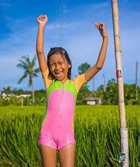 young happy and carefree beautiful child 7 or 8 years old outdoors having shower at a beautiful rice terrace playful under the water wearing cute girl