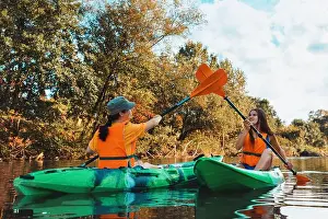 Kayaking Prints: Two young happy women are kayaking and high-fiving on the oars. Outdoor activity