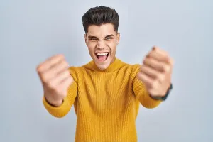 Furious Prints: Young hispanic man standing over blue background angry and mad raising fists frustrated