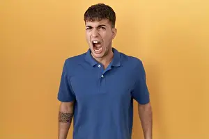 Enraged Prints: Young hispanic man standing over yellow background angry and mad screaming frustrated and furious