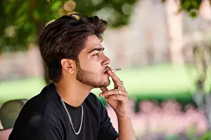 Smoker Prints: Young indian man smoker portrait in black t shirt and silver neck chain in public park