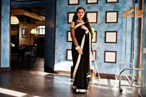 Saree Prints: Young indian woman wear at elegant black saree posed on restaurant against wall with frames