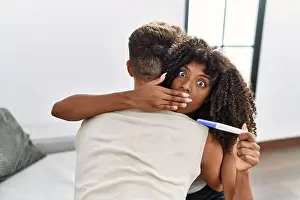 Shocked Prints: Young interracial couple holding pregnancy test result covering mouth with hand