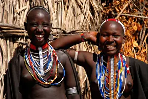Female Friend Prints: Two young laughing girls of the Arbore people wearing many colourful necklaces in front of a hut Ethiopia