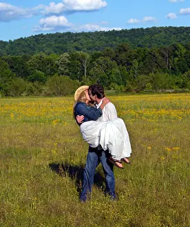Kissing Prints: Young man carries wife across flower filled field