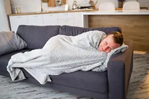 Fever Prints: Young man with flu, sitting on the couch at home, wrapped in a blanket