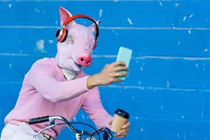 Taking Prints: Young man with pig mask taking selfie while listening music through headphones on bicycle