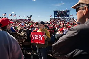 Republican Prints: A young man poses for a photo holding a Trump Vance sign at an outdoor rally during the 2024 presidential campaign