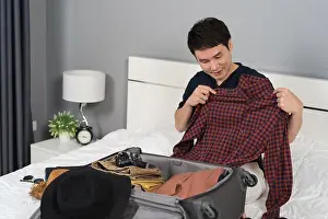 Stuff Prints: young man preparing and packing clothes into suitcase on bed at home