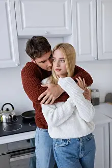 Sweaters Prints: young man in red sweater hugging blonde girlfriend in kitchen, stock image