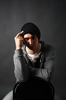 Fatigue Prints: the young man sitting on a chair in a gray hoodie and a black hat holding his hand to his head in the shade