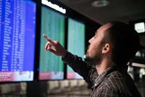 Delay Prints: Young man traveling, pointing finger on train timetable in railway station