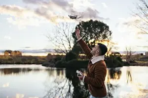 Remote Control Prints: Young man using a drone near a lake to record and photograph the landscape