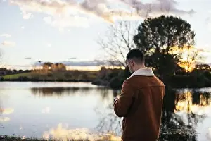 Remote Control Prints: Young man using a drone near a lake to record and photograph the landscape