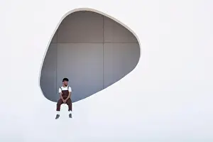 25 30 Years Prints: Young man wearing bib overalls sitting on hole in wall