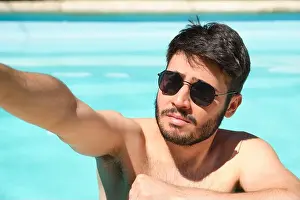Posh Prints: Young man wearing sunglasses taking a selfie with a smartphone in a swimming pool