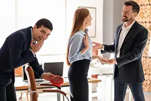 Cushion Prints: Young man with whoopee cushion playing a prank on his colleague in office