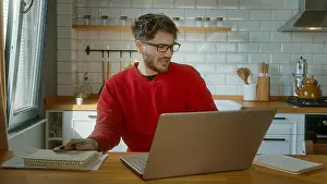 Annoyed Prints: Young Man Working on Laptop in a Bright Modern Kitchen