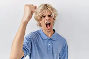 Punching Prints: Young modern man standing over isolated background angry and mad raising fist frustrated