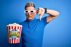 Discontent Prints: Young modern man watching cinema movie wearing 3d glasses and eating popcorn with angry face