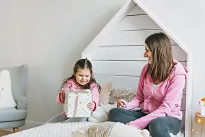 Toys Prints: Young mother and cute girl in pink family looks hoodie on the bed in children room